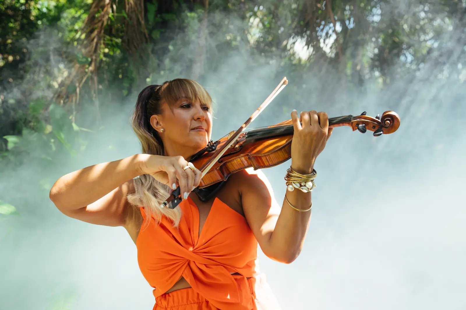 Playing violin in an orange dress, in the mist among the trees