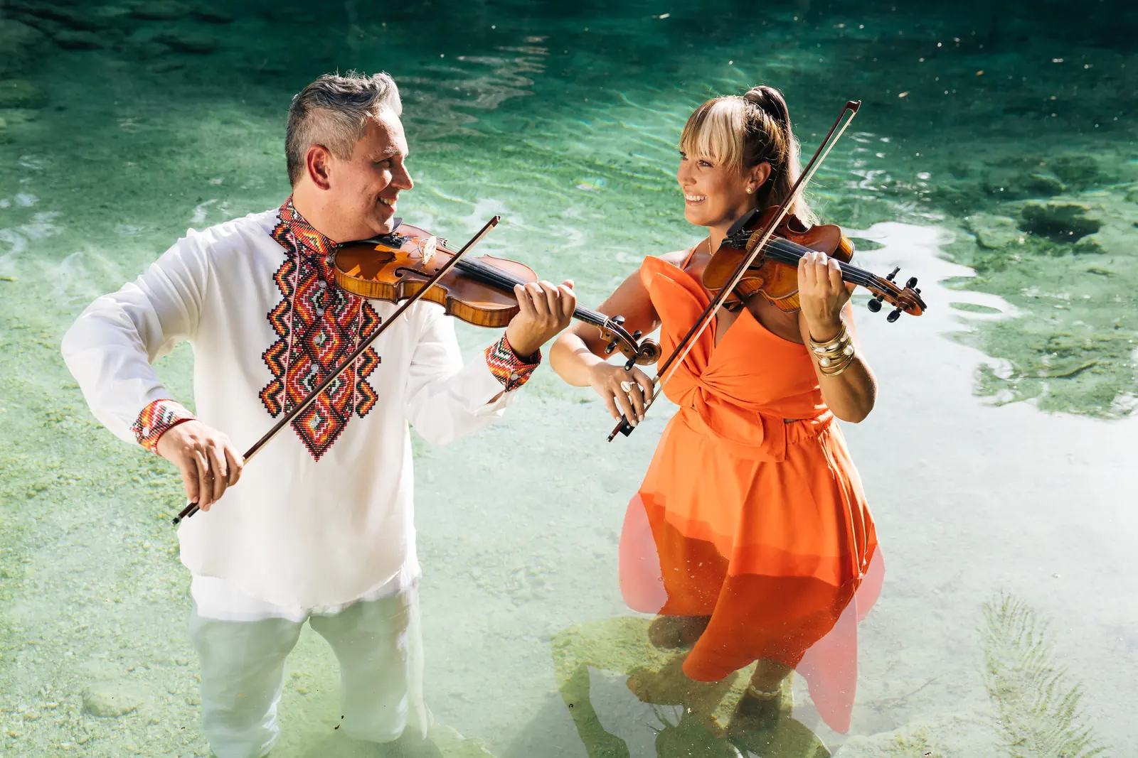Tania and Abraham playing violin together in a clear river